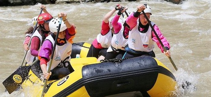 sixe peple in pink shirts and white life jackets rowing a yellow inflatable boat in rough water.