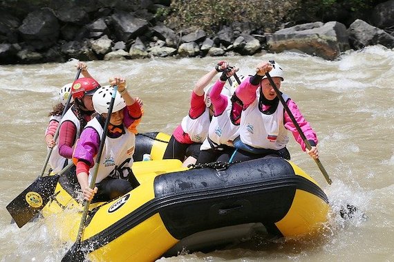 sixe peple in pink shirts and white life jackets rowing a yellow inflatable boat in rough water.