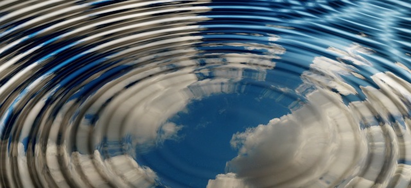 a body of water with circular ripples and clouds reflected in the surface.