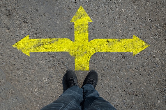 Yellow arrow pointing right, left and straight on asphalt with a feet in black shoes at the edge.