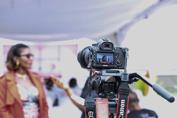 a video camera on a tripod shooting a scene of a woman and others which is out of focus.