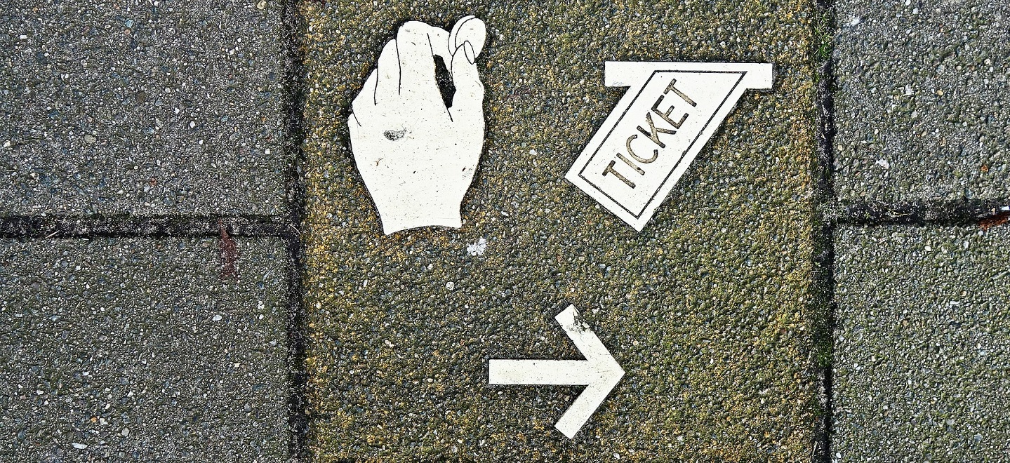 Decals on a sidewalk showing a hand putting a coin in a slot, a ticket coming out of another slot, and and arrow