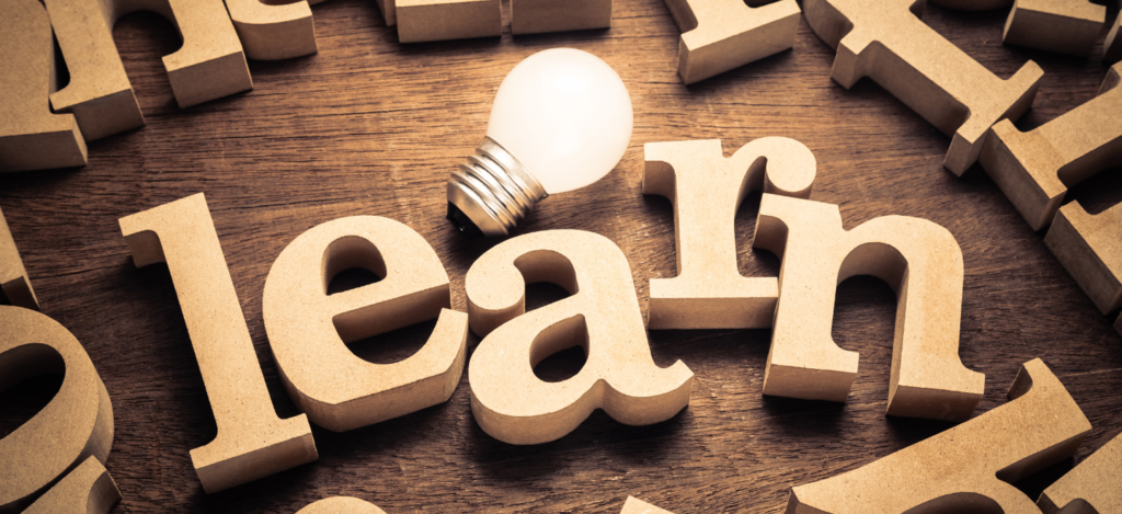 letters cut out of wood scattered around, at the center they spell learn with a light lightbulb next to them.
