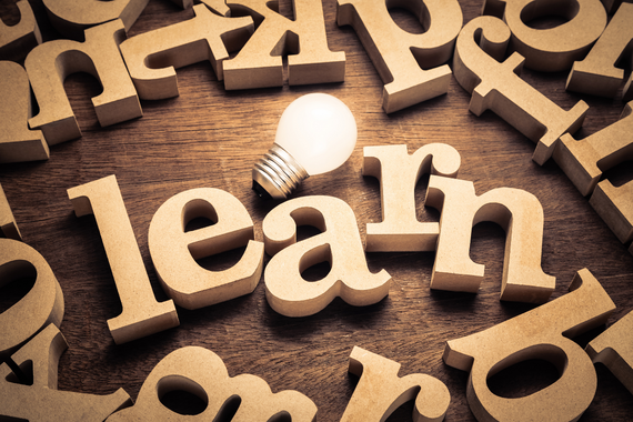 letters cut out of wood scattered around, at the center they spell learn with a light lightbulb next to them.