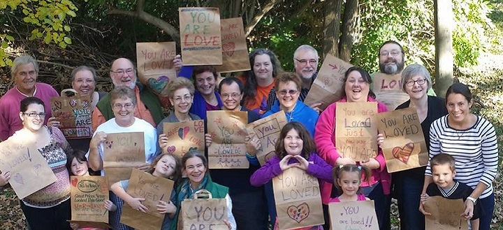 A multi-age group holding signs saying "you are loved"