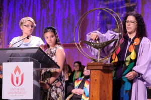 Marta Valentin lighting the UUA chalice at General Assembly with Alison Chase and Jaiya Valentine Chase watching on