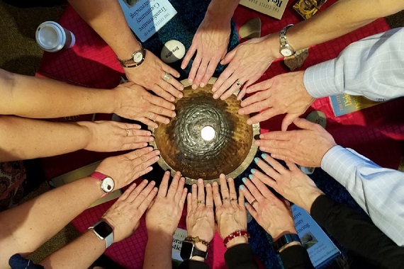 14 hands touching the rim of a large gold chalice