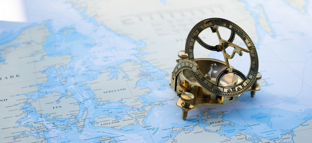 An antique navigation device sitting on a world map.